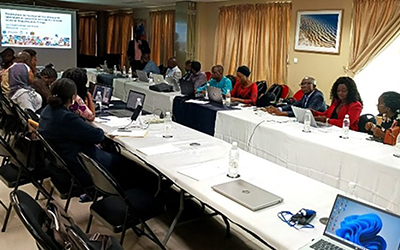 Plenary session in the Congo. People sitting around a table watching a screen projecting a presentation.