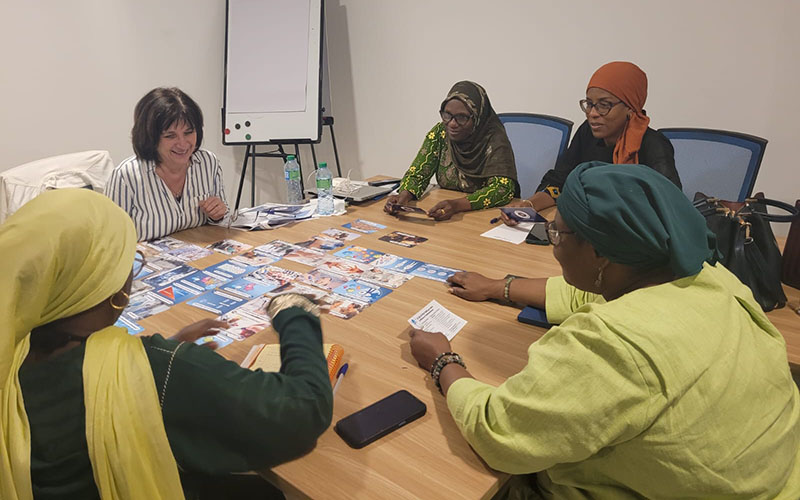 In a meeting room, five people are seated around a table, holding the cards of the AMR fresco in their hands.